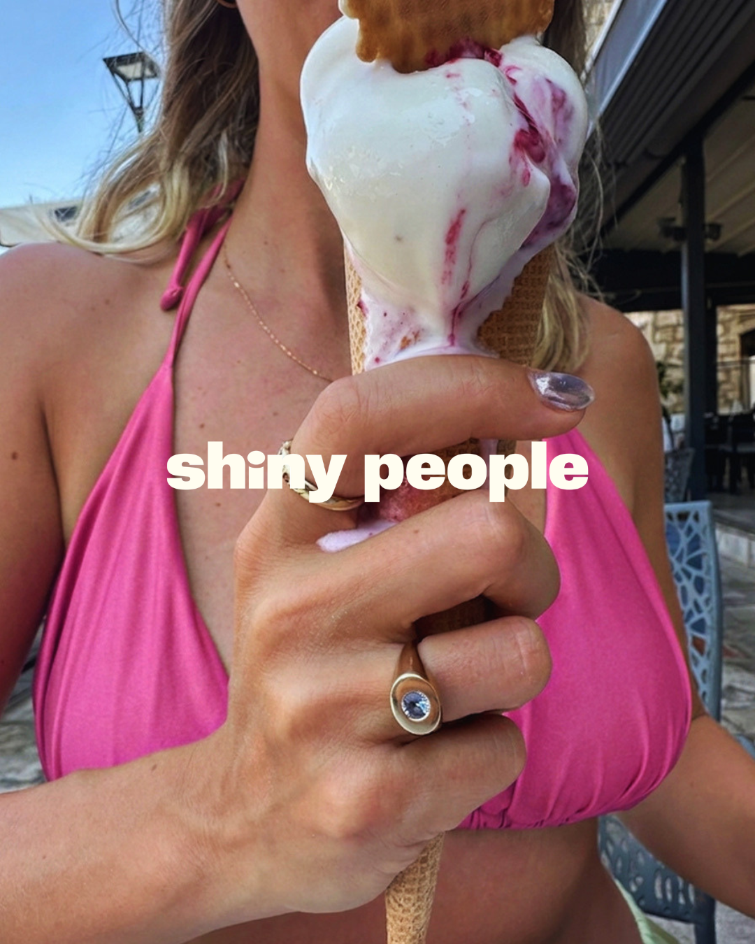 A close-up lifestyle shot of a woman in a pink bikini holding an ice cream cone outdoors. She is wearing a gold ring with a blue stone on her finger, and a white text overlay reads 'shiny people'.

