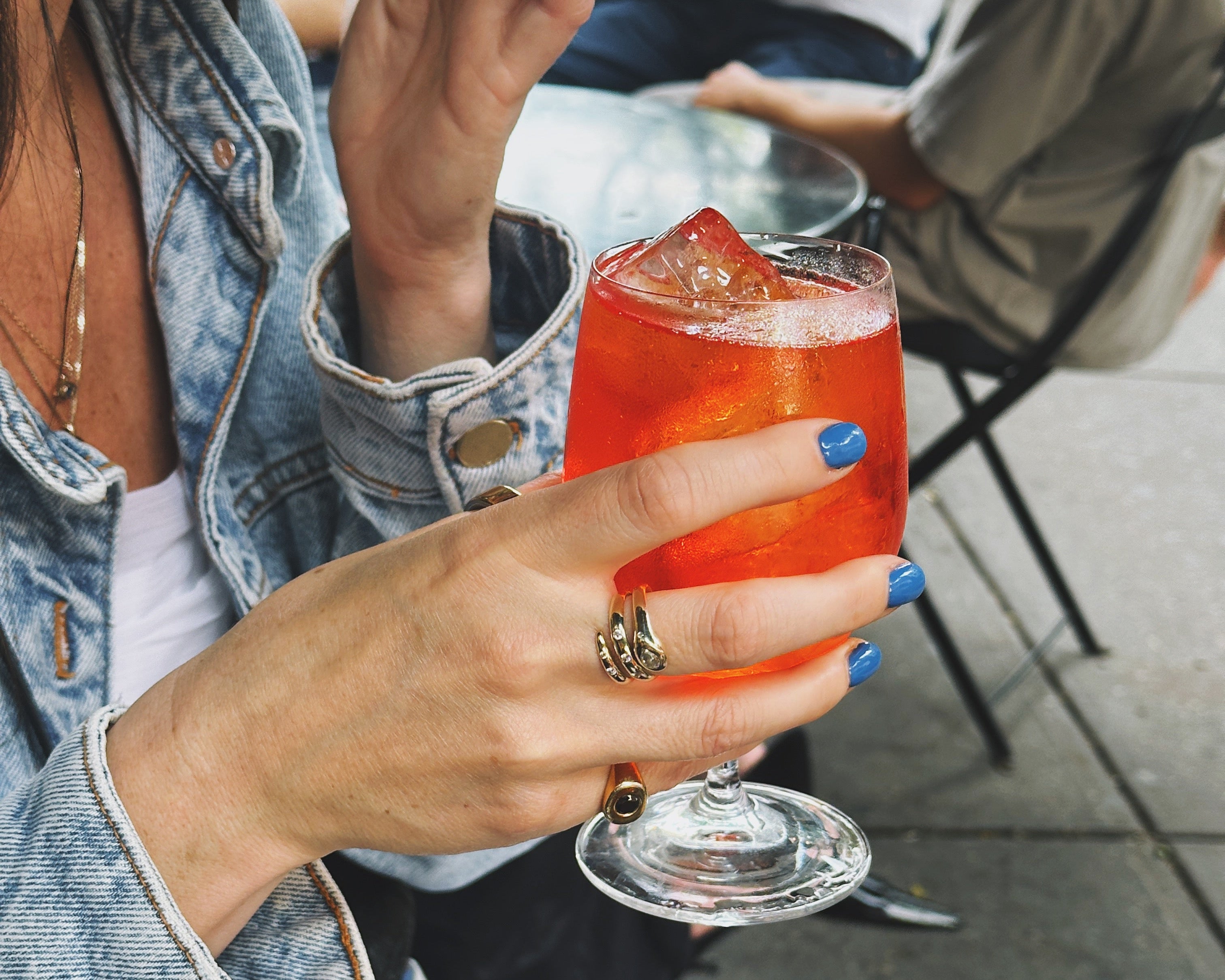 Person wearing diamond snake ring and signet ring while drinking aperol 